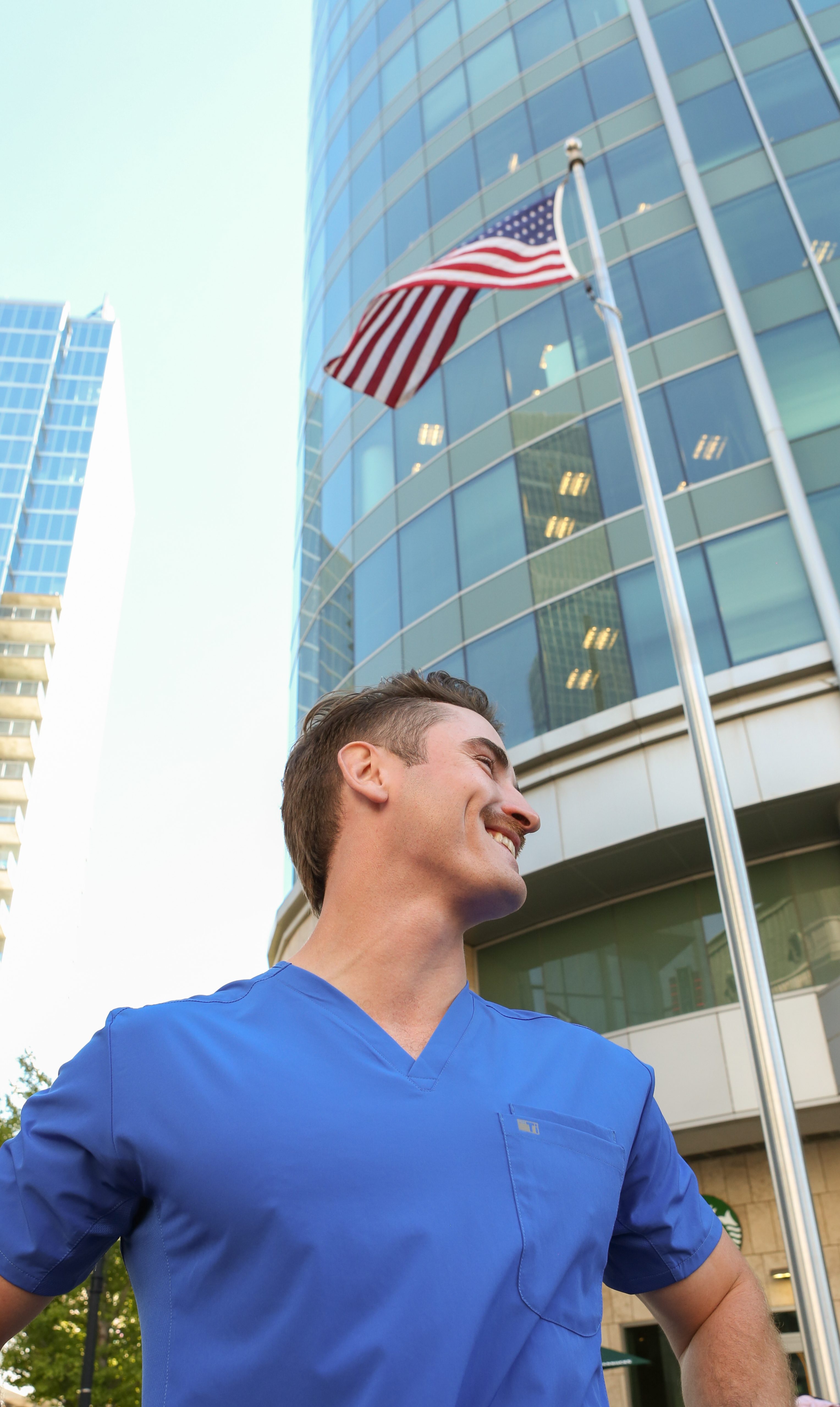 Man in Royal Blue TiScrubs Double-Pocket Top in City by American Flag