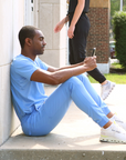 Man Texting on Phone Sitting in Ceil Blue Men's Scrub Joggers and Double-Pocket Scrub Top
